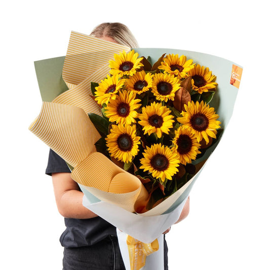 Beautiful Dozen Sunflower Bouquet with bright yellow blooms wrapped in paper and held by a florist for same day flower delivery
