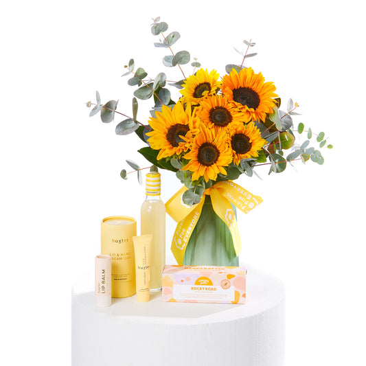 Sending Sunshine Hamper with bright sunflowers in a glass vase alongside a yellow candle lip balm and rocky road treat for same day flower delivery